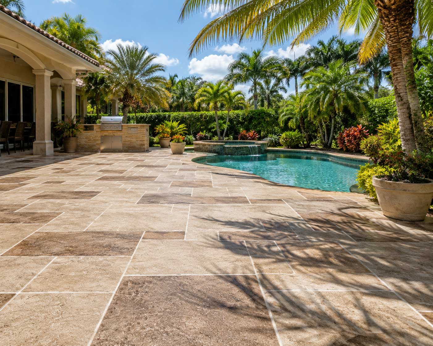 Concrete overlay patio with a tan travertine finish beside a free-form pool, spa, and outdoor kitchen in Palm Beach and Broward County