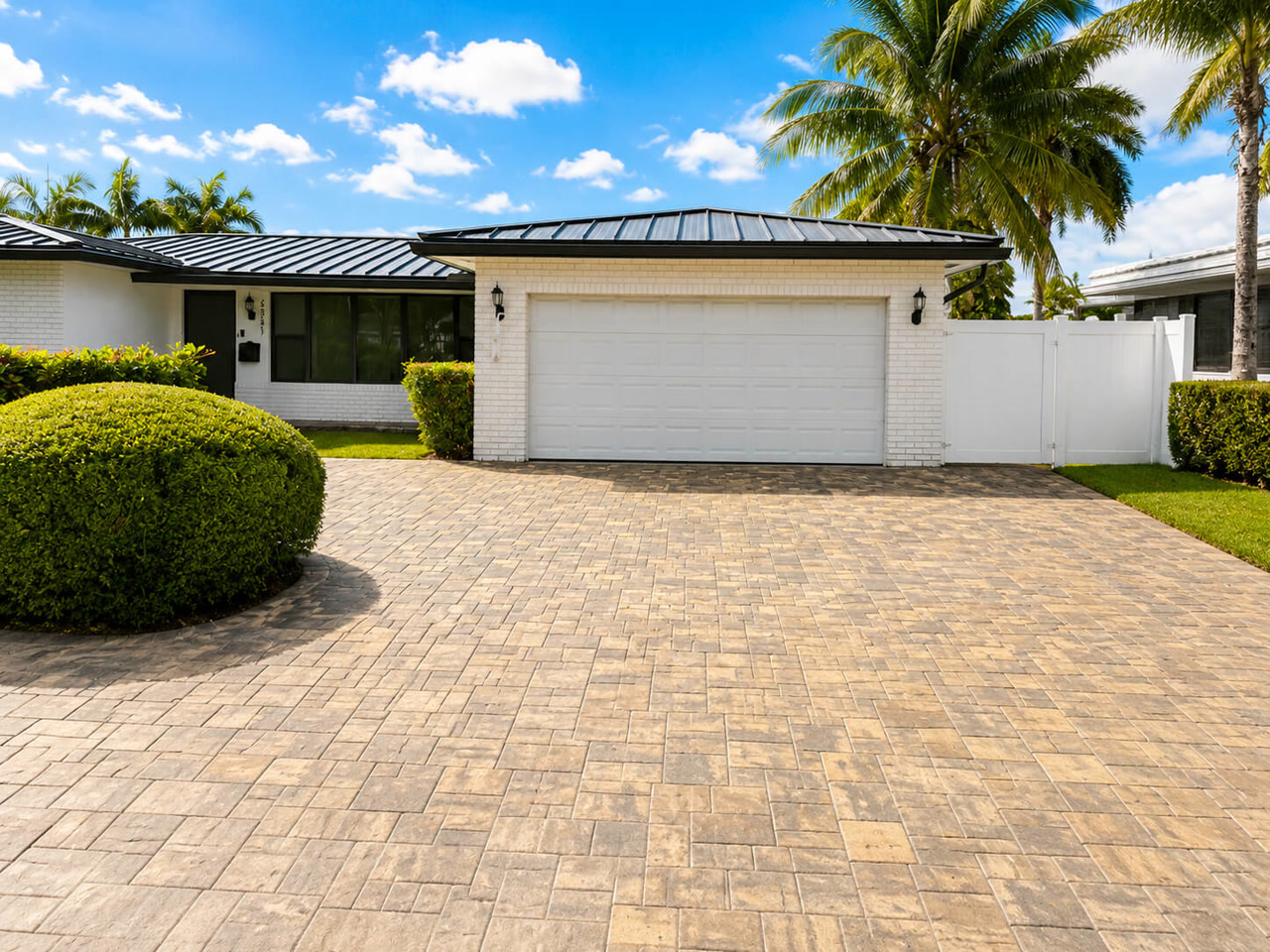 Beige running bond paver driveway at a white brick home with a black standing seam metal roof on a Loxahatchee property
