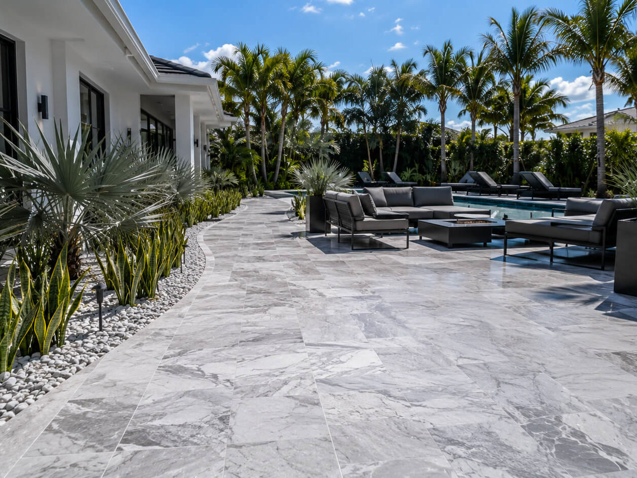 Gray marble paver patio curving along a modern home to a poolside lounge at a Juno Beach residence