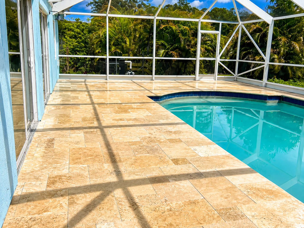 Sand toned travertine paver pool deck under a white screen enclosure at a Boca Raton residence, with dark blue tile coping along the pool