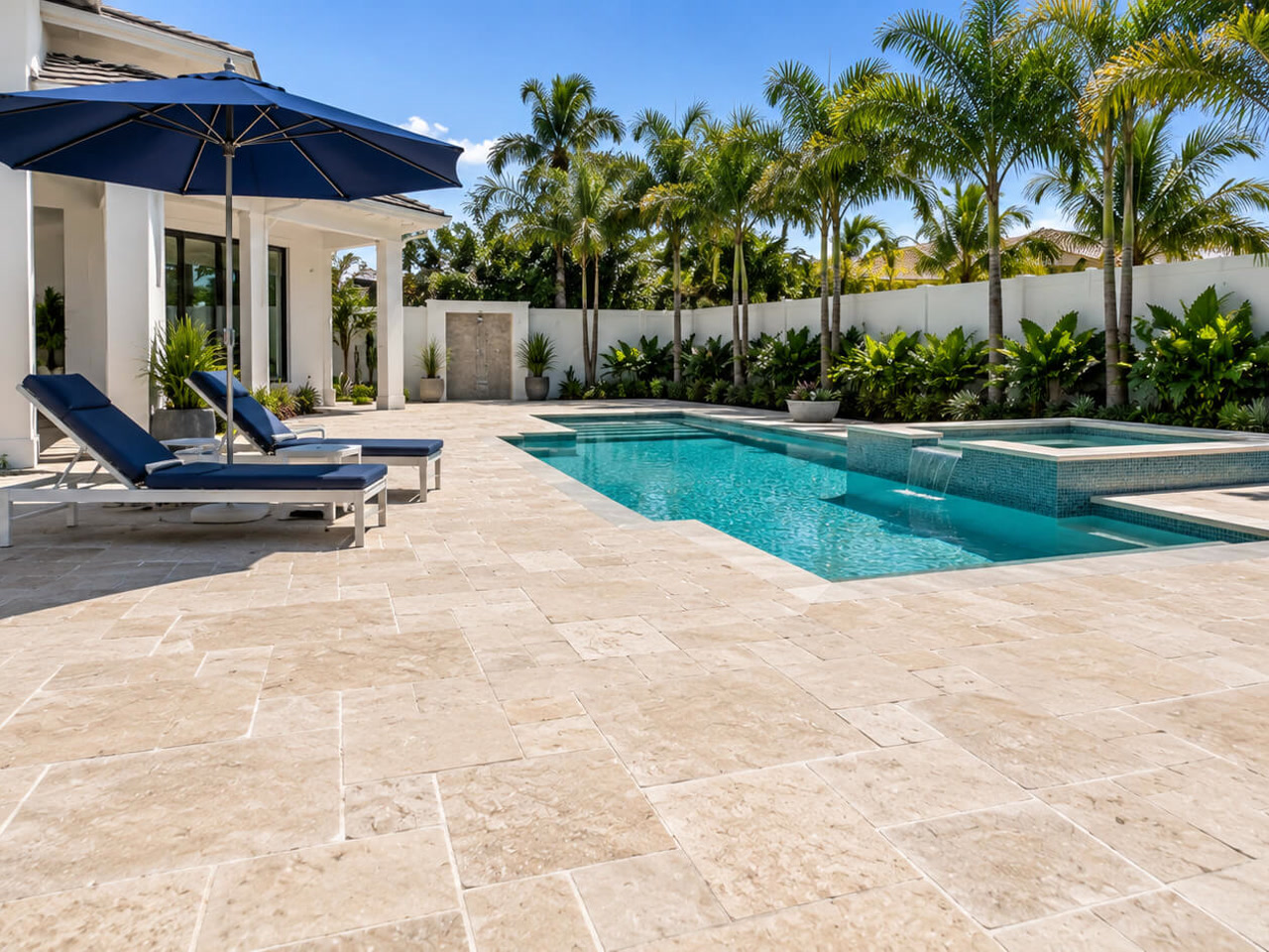 Beside a pool with a raised spa and sheer descent, an ivory travertine paver deck in a French pattern in Deerfield Beach