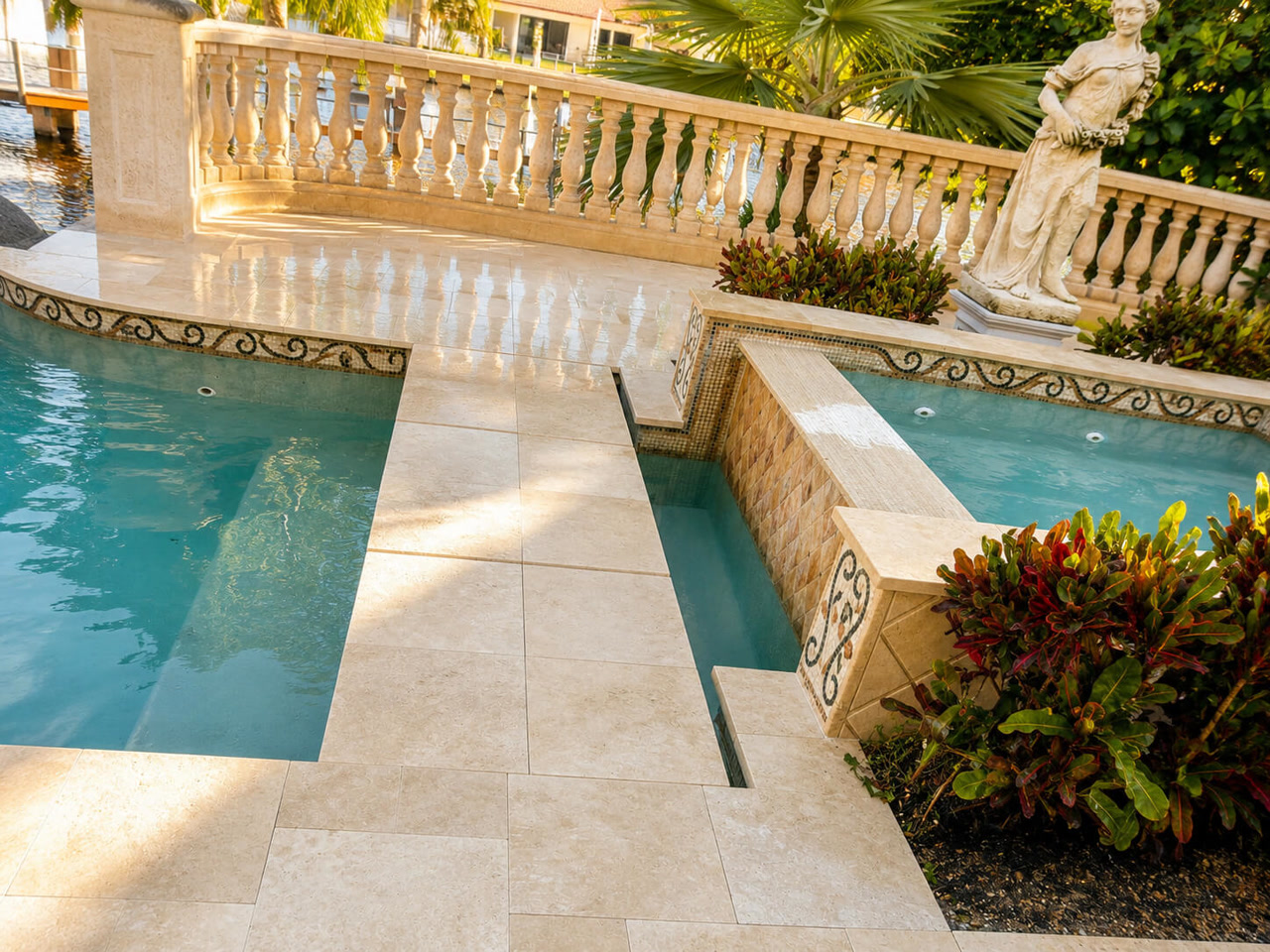 Ivory paver pool deck with a stone balustrade and mosaic tile spillway at a Juno Beach waterfront estate
