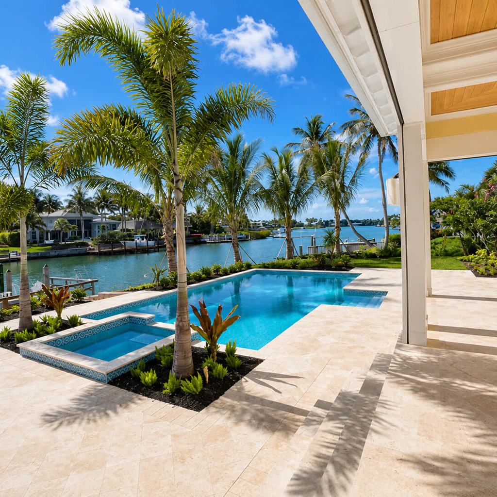 Ivory travertine paver deck connecting a covered lanai to a pool and spa on a waterfront canal lot at a Loxahatchee residence