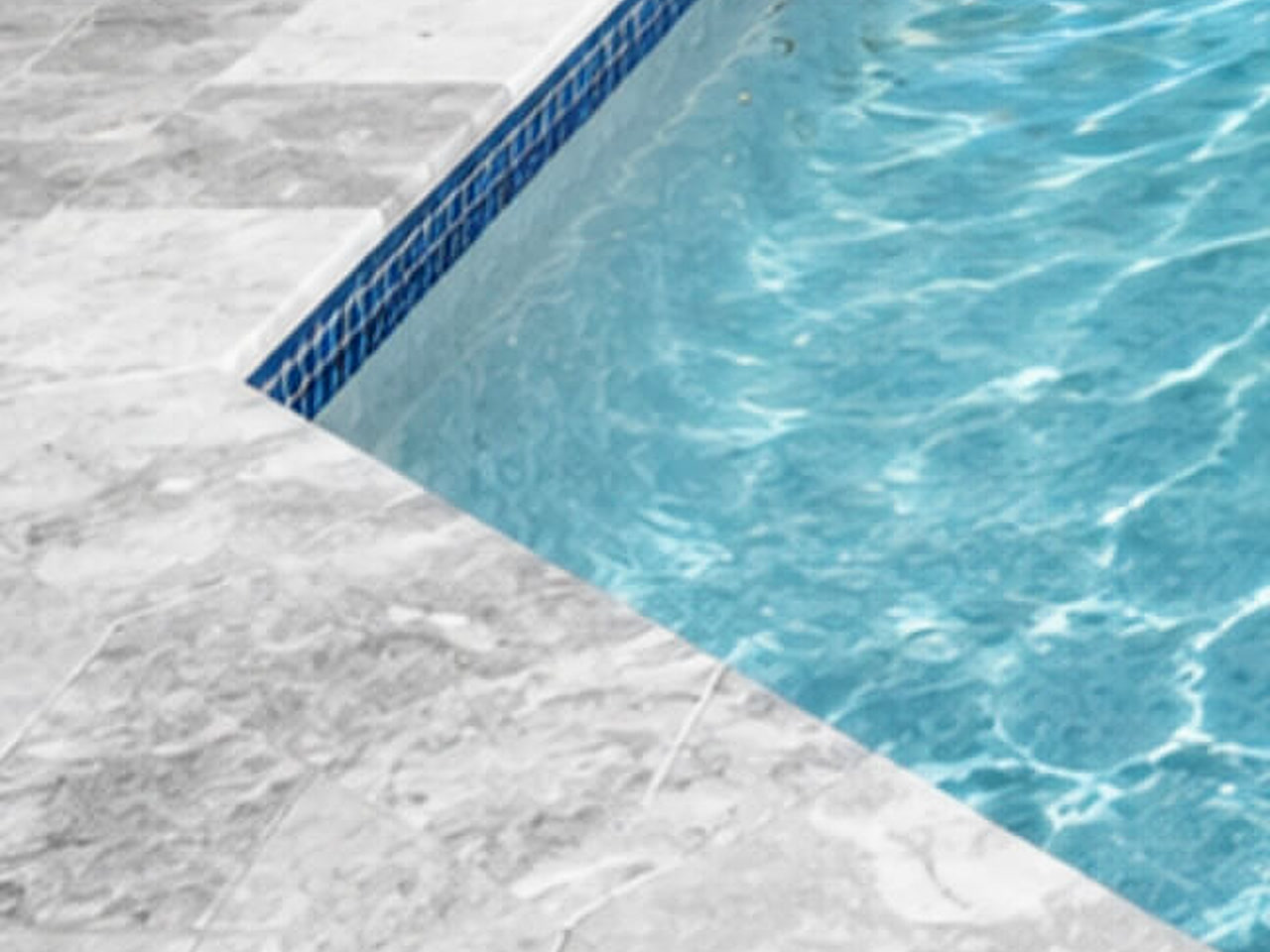 Pool coping with a squared gray marble profile over a cobalt mosaic waterline band on a Boca Raton property