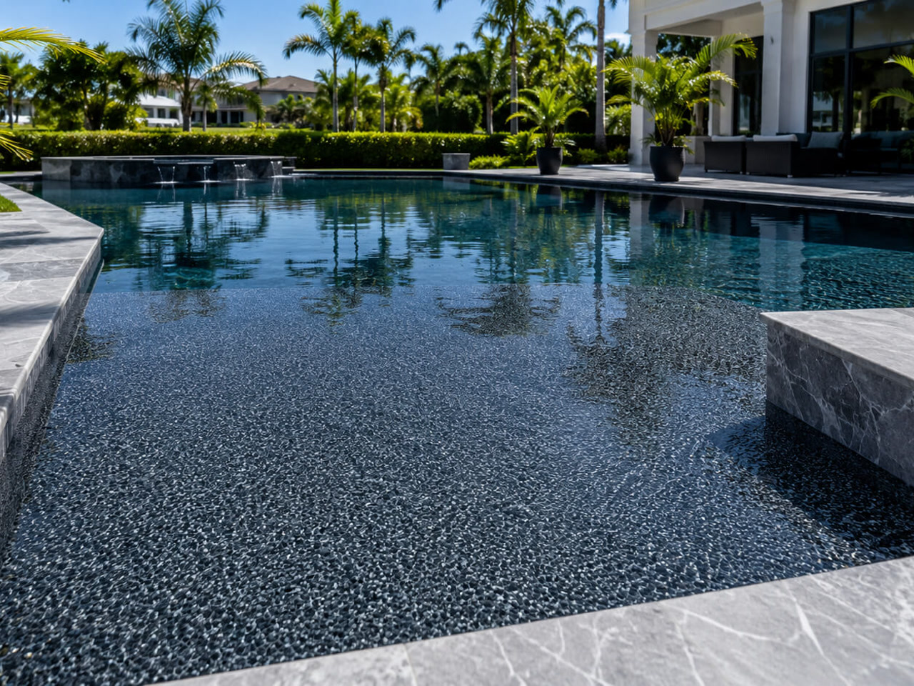 Pool finish renovation with a dark charcoal pebble interior and gray marble coping at a Hypoluxo residence