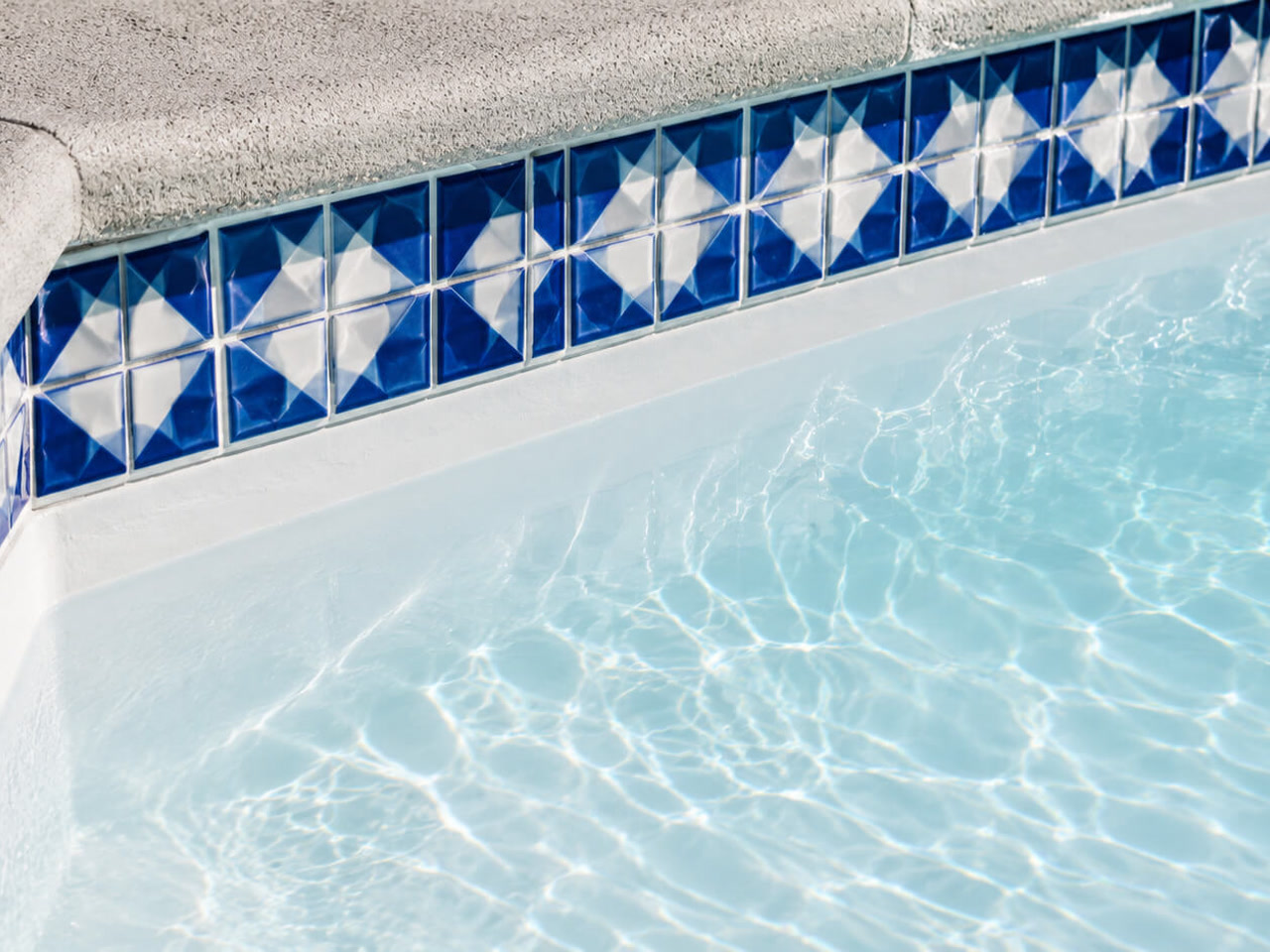 Classic white plaster finish under a blue and white diamond patterned tile border and textured concrete coping for a Boynton Beach homeowner