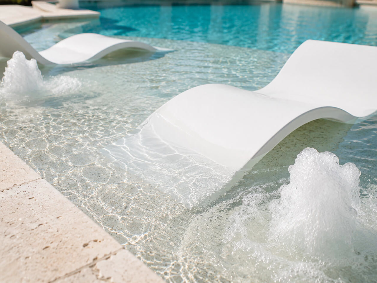 White in water loungers on a shallow sun shelf with bubblers churning on either side at a Juno Beach pool