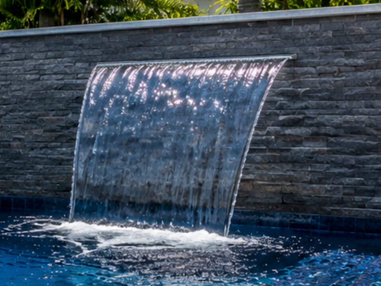 Sheer descent waterfall blade falling from a gray stacked stone wall into a deep blue pool in Jupiter