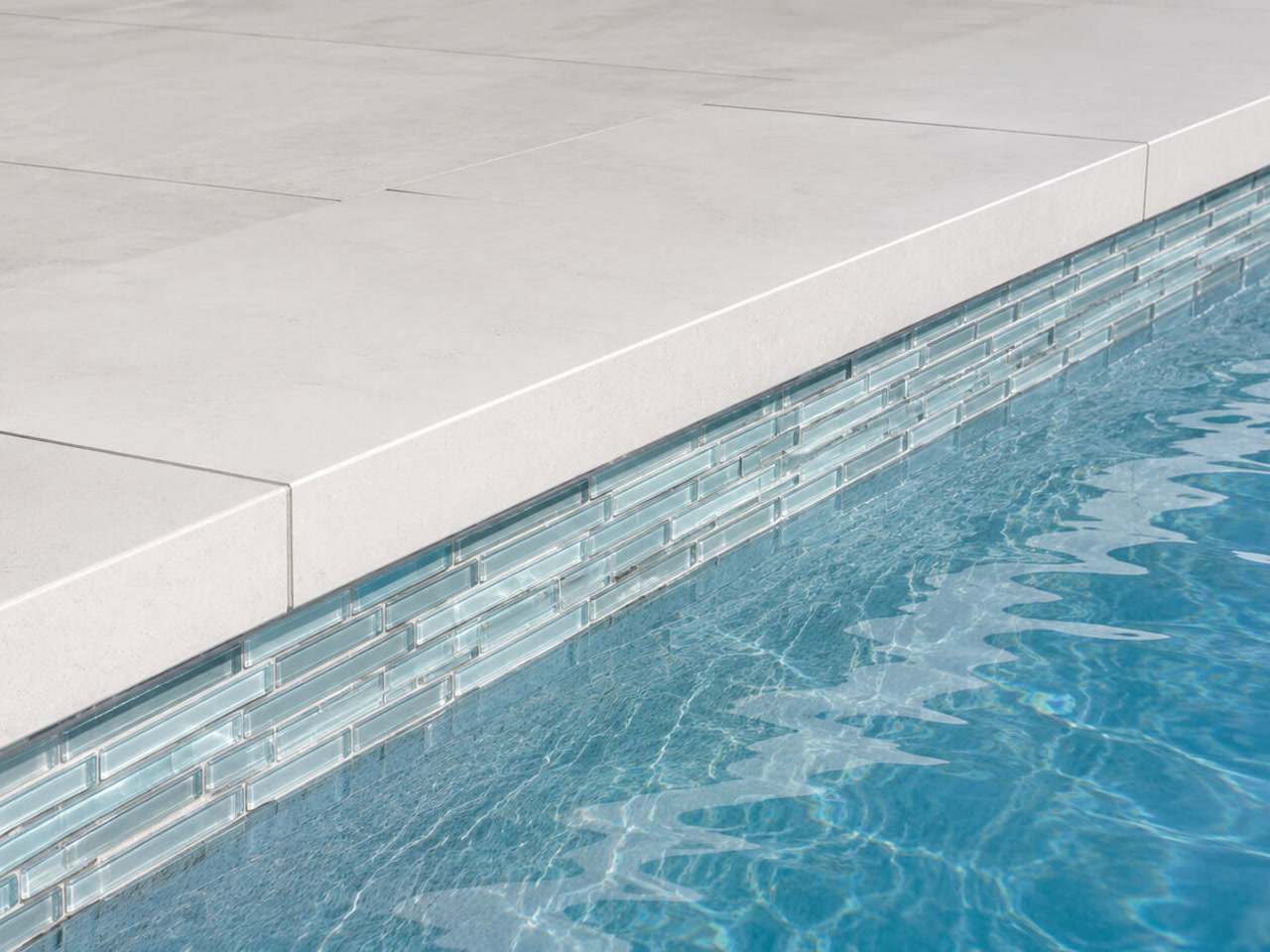 Squared off light stone pool coping over linear pale blue glass waterline tile at a Deerfield Beach home