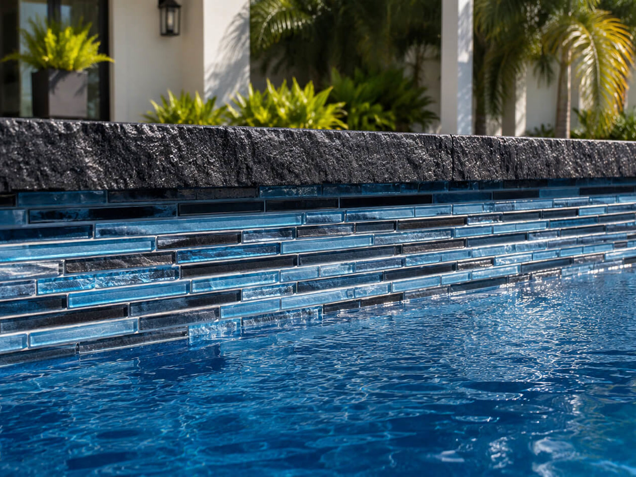 Finished pool edge with a rough cut black stone coping over linear blue glass tile at a Jupiter Island residence