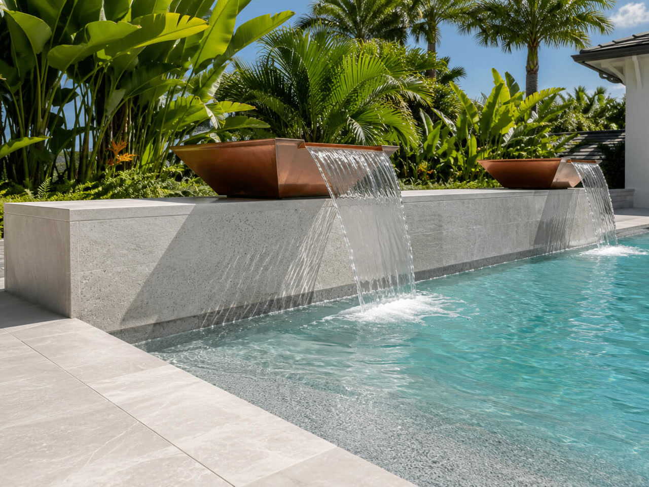 Copper scupper bowls spilling over a light stone wall into a pool framed by tropical planting
