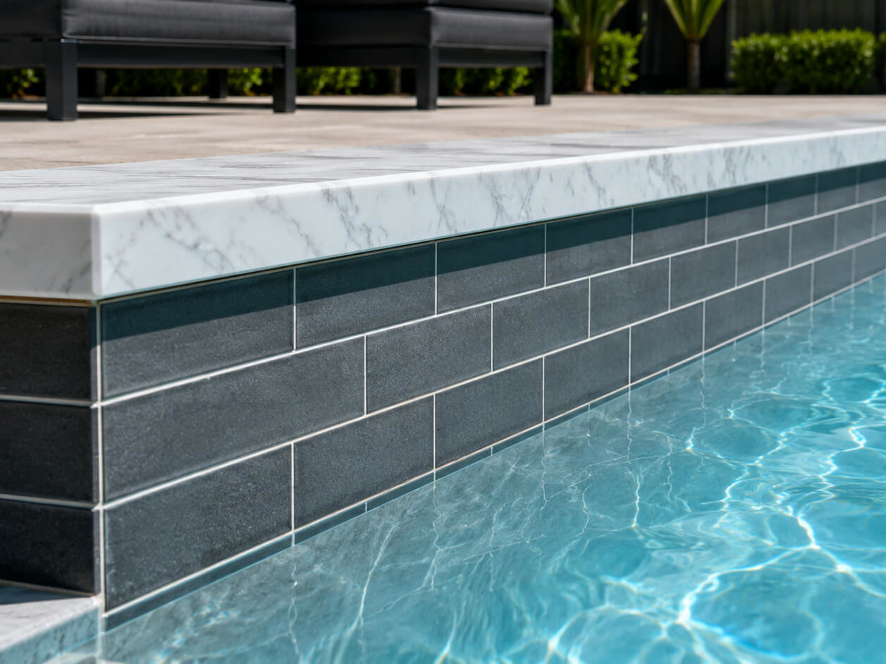 White marble coping cap over charcoal subway tile along a pool wall